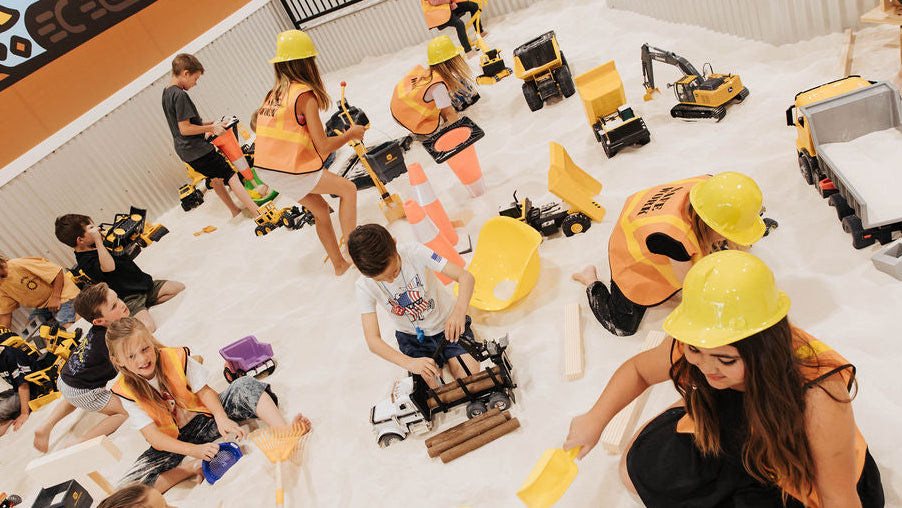 Children playing with construction toys in a sand pit at a play center.